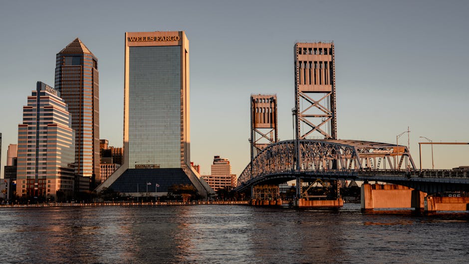Stunning view of Jacksonville, FL skyline at sunset with iconic bridges and modern skyscrapers reflecting on the water.