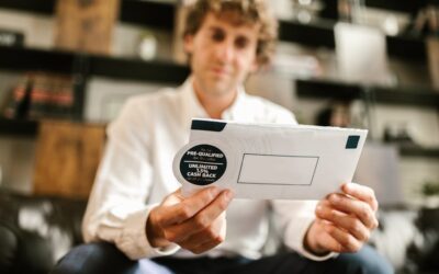A man sitting indoors, reading an envelope with a cash back offer, blurred background.