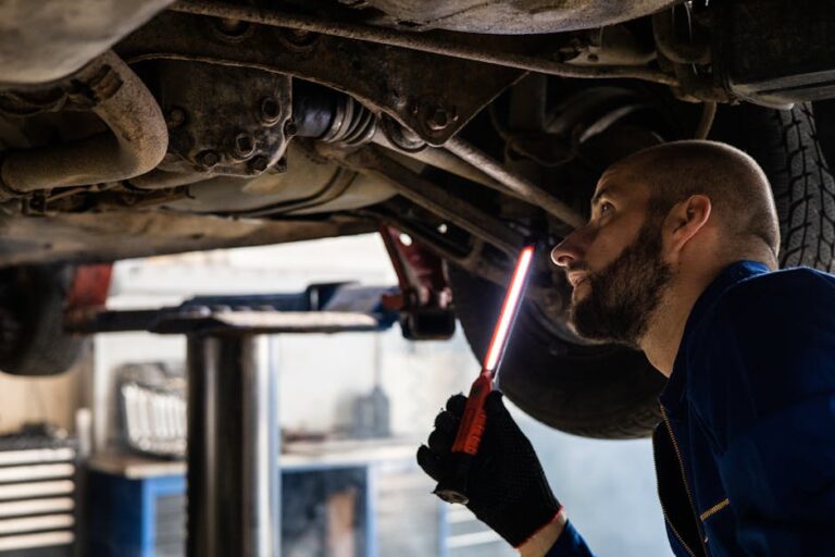 Mechanic using light to inspect vehicle undercarriage in workshop for maintenance.