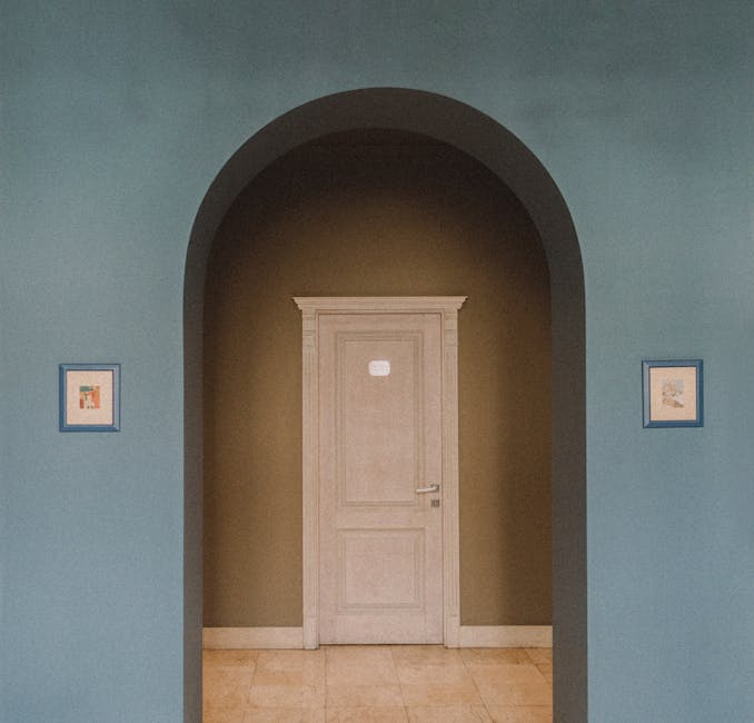 Interior focus on an archway leading to a classic door, flanked by framed artwork.