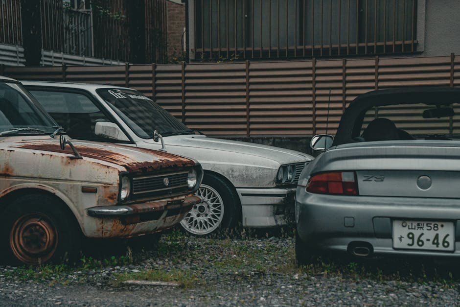 A rusted vintage car alongside modern vehicles in a gritty urban backdrop, highlighting contrast.